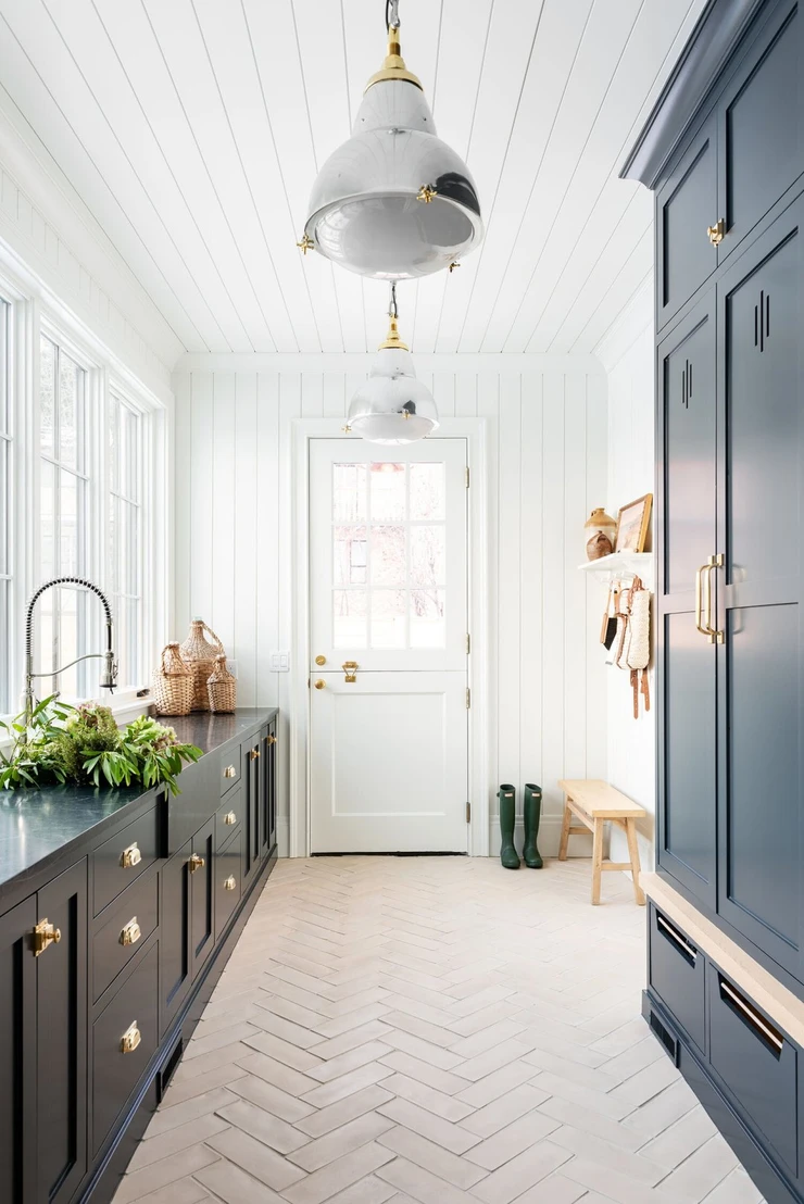 navy blue cabinets dark stone counter herringbone brick tile dutch door polished chrome and brass pendant lights shiplap ceiling and shiplap walls wood bench hunter rain boots wall hooks