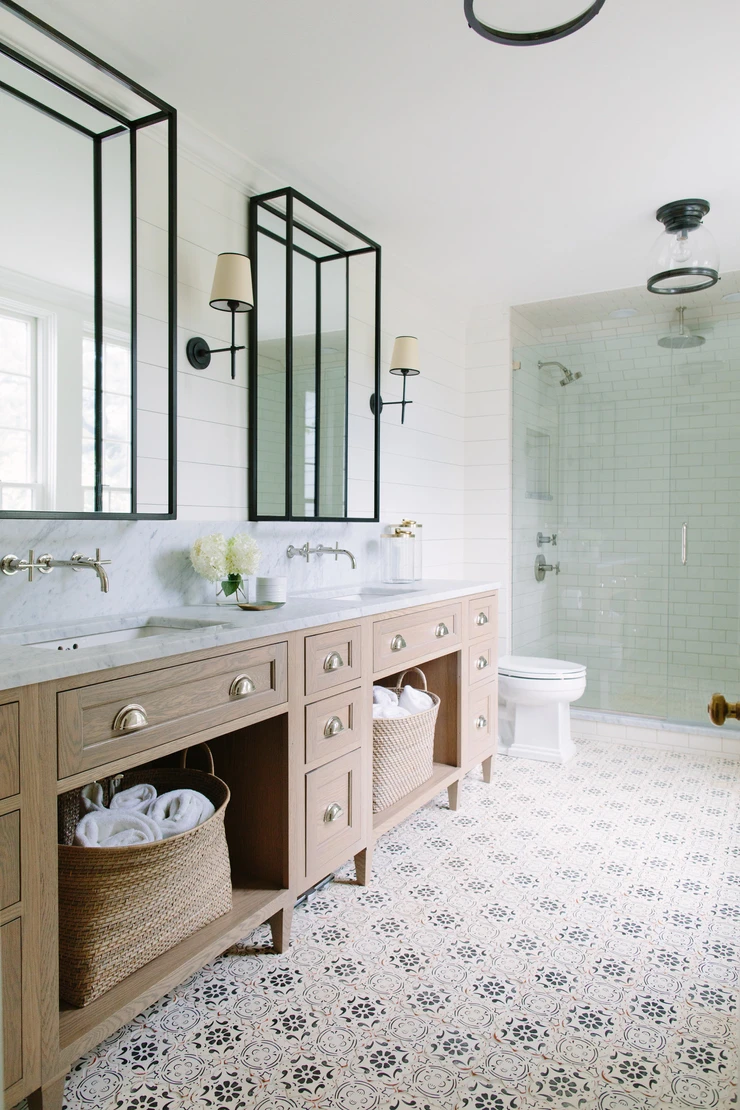 marble countertop concrete patterned tile floor bathroom wood double sink vanity open storage baskets with towels wall mounted hardware black framed mirrors wall sconces walk in tile shower subway shiplap walls nautical light fixture