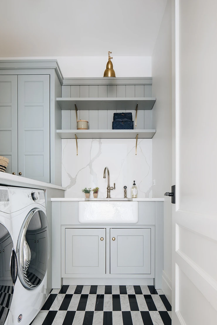 laundry room with black and white rectangular floor tiles farmhouse sink brass hardware storage brass sconces white door front load washer and dryer countertop