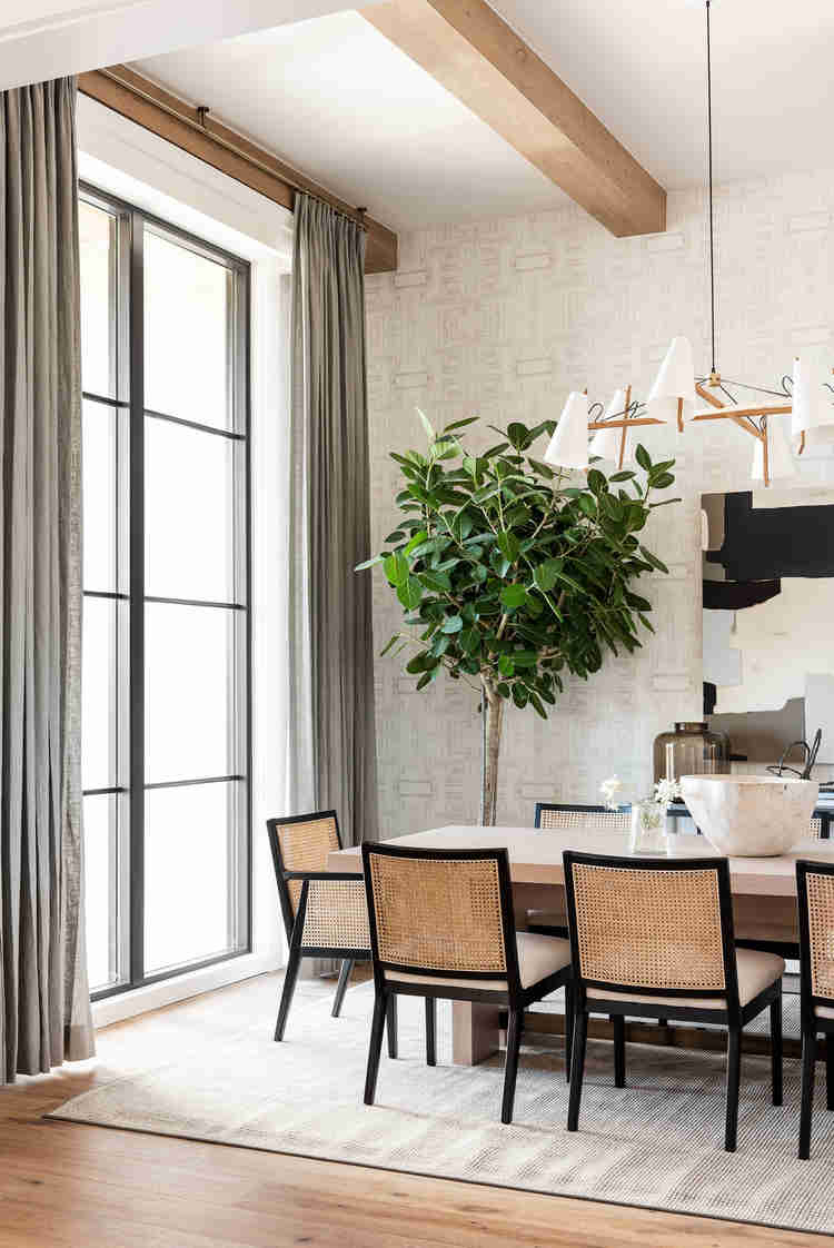 wood beam accented ceiling wallpaper soft grey drapery black framed windows dining table with black framed chair on beige area rug hardwood floors floor plant